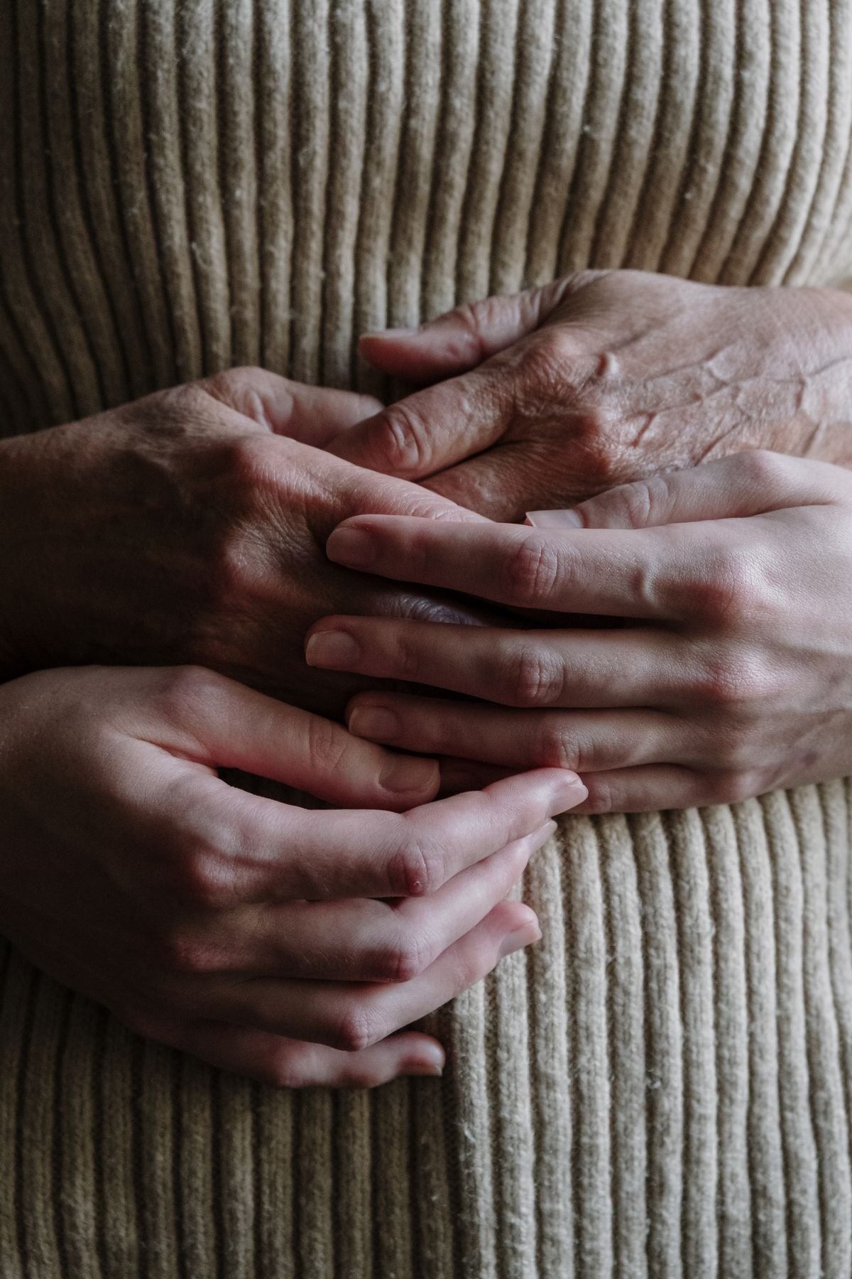 Mãos de pessoas de diferentes idades em gesto de cuidado; fotografia de banco sem rostos.